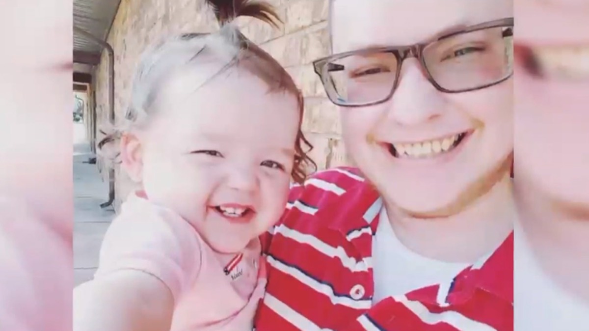 Dustin Parker smiling in a red striped shirt, holding one of his young children who is also smiling.